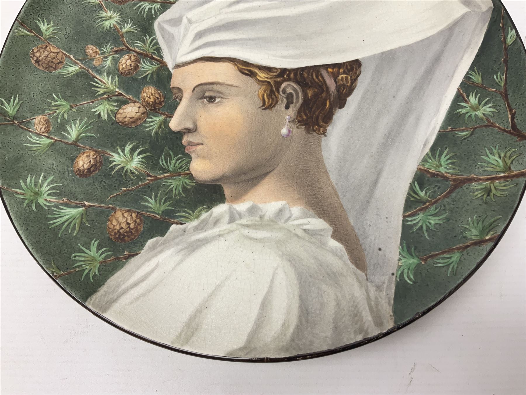 19th century continental pottery charger, depicting a woman in a white veil with pinecones on a green ground, with indistinct signature to the back, D31cm