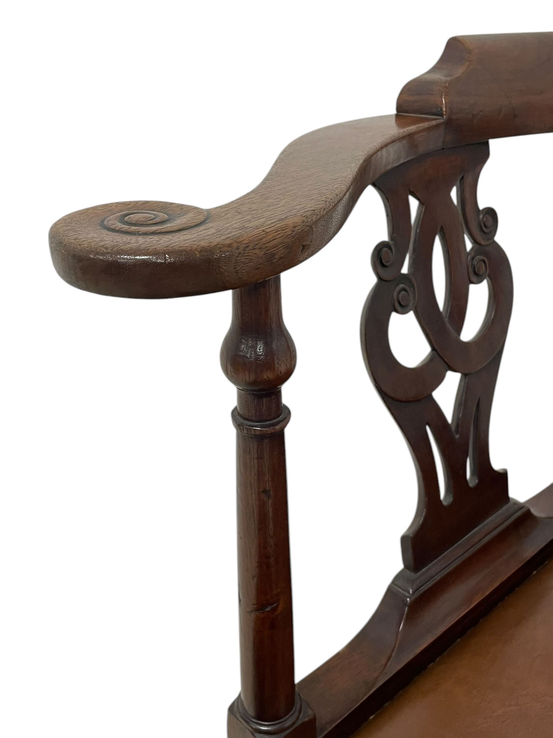 George III mahogany corner elbow chair, curved back rest and shaped arms with scroll carved terminals, on turned supports and pierced scroll carved interlaced splats, drop-in seat upholstered in brown leather, on square supports with inner chamfer and outer moulding 