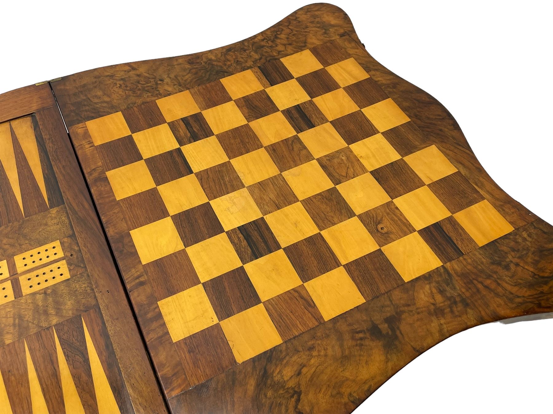 Victorian inlaid figured walnut games table, the serpentine fold-over top inlaid with scrolling foliate decoration, the top opens to reveal cribbage, backgammon and chess boards, single drawer over sliding storage well, on twin pillar supports united by double turned stretchers, on foliage carved out-splayed supports with brass and ceramic castors 