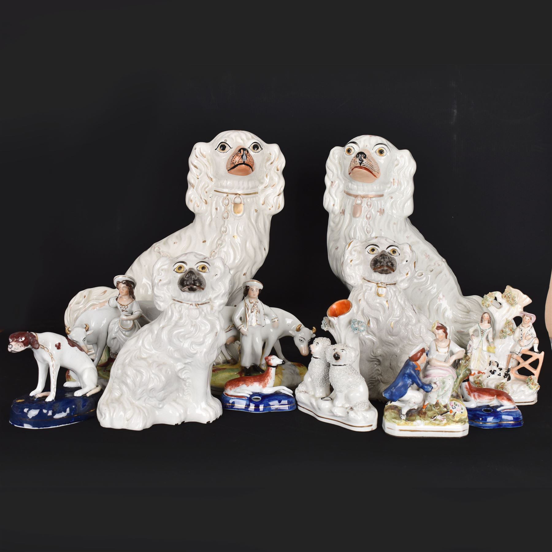 Staffordshire and Staffordshire style figures, to include a chained hound upon a blue oval base in the manner of Samuel Alcock, two pairs of seated Spaniels, a pair modelled as male figure and milk maid with cows, pair of recumbent Greyhounds, etc.