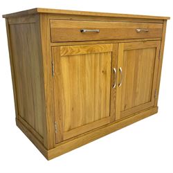 Contemporary light oak sideboard desk, rectangular top with full length drawer, hinged front panel revealing pull-out keyboard tray, over two panelled doors enclosing an assortment of shelves and compartments with cable management holes, on plinth base