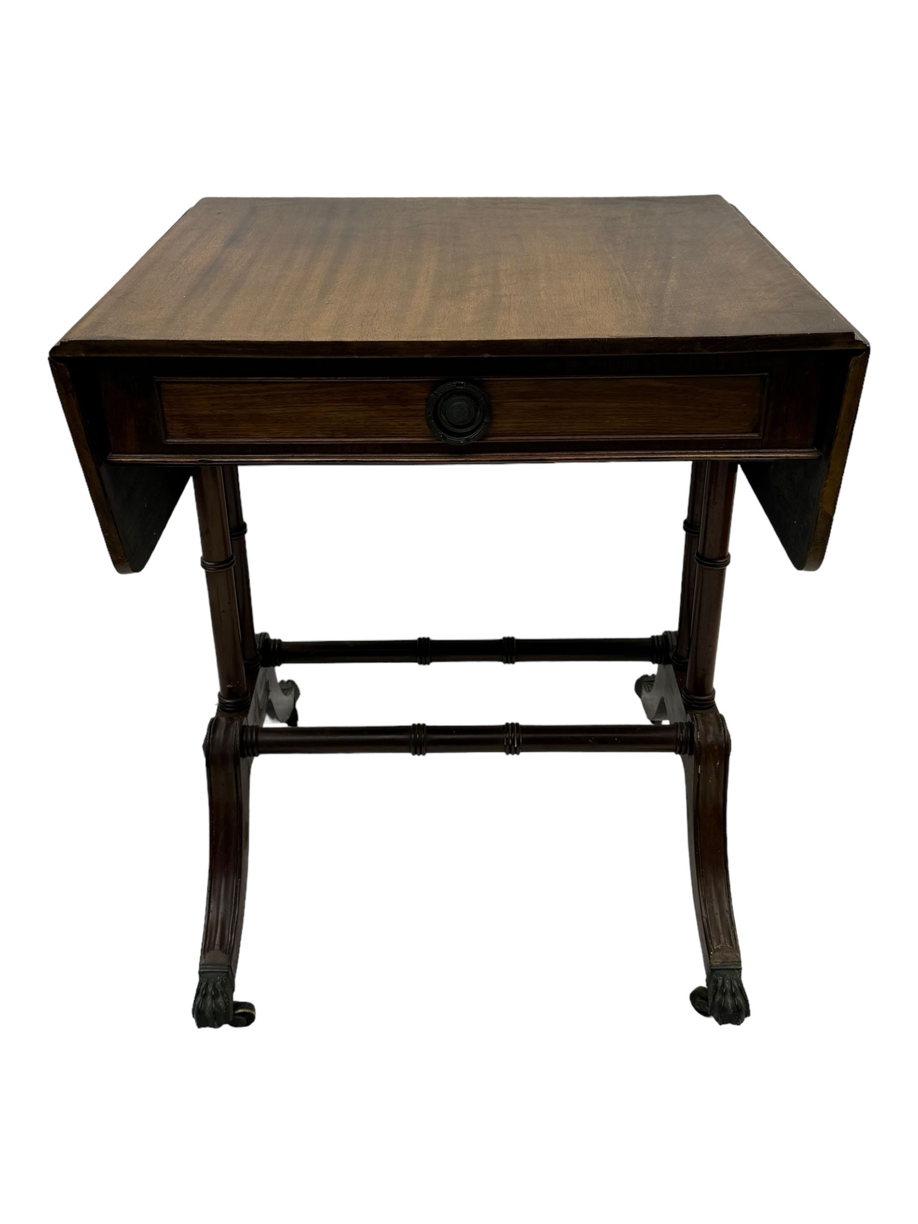 Mahogany drop-leaf sofa table, rectangular top over single frieze drawer with carved rosette handle, twin turned columns united by twin stretchers, on splayed supports terminating in paw feet with castors