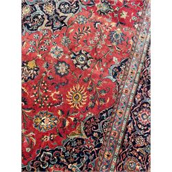 Persian Kashan crimson ground carpet, central rosette medallion on a field of trailing foliate branches decorated with palmettes, scrolling border with repeating plant motifs and flower heads, enclosed within floral pattern guard stripes