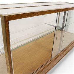 Early 20th century glazed oak and brass bound shop's display cabinet or haberdashery cabinet, fitted with two sliding glass doors, two glass shelves on chromed metal supports, black finish block feet