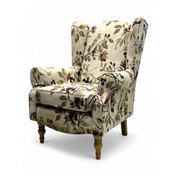 Hardwood-framed wingback armchair, upholstered in cream floral pattern fabric, on turned front feet