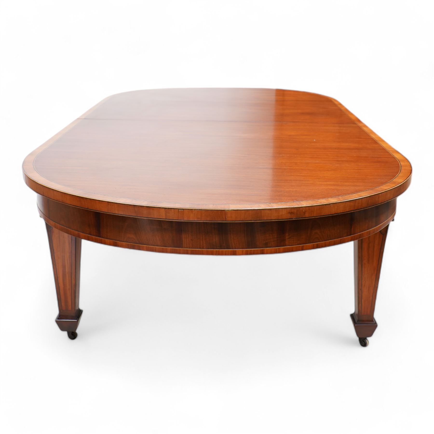 Late 19th to early 20th century mahogany and satinwood banded dining table, telescopic extending action, with three additional leaves, figured frieze rails over square tapering supports with spade feet, inlaid with satinwood panels, on brass castors 