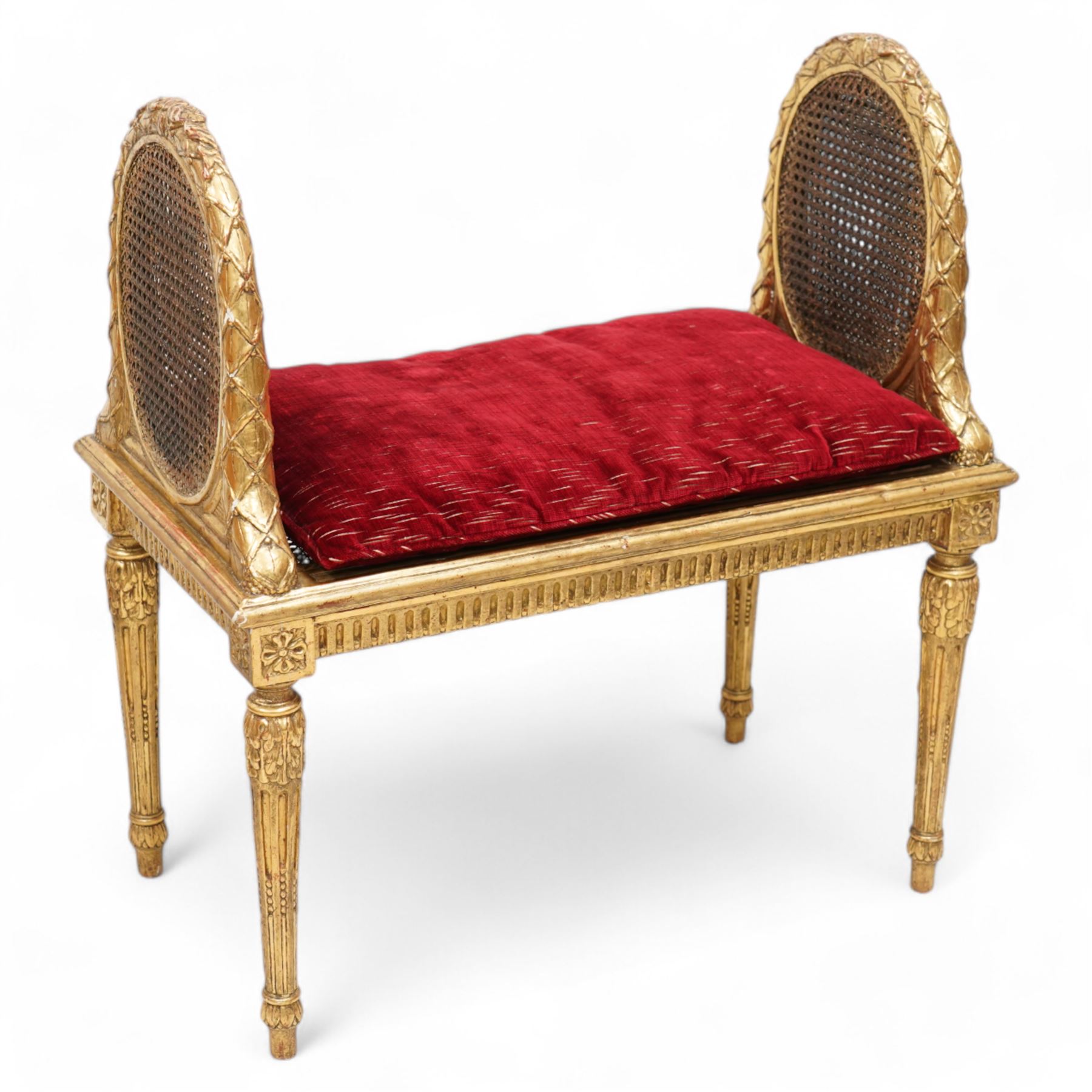 Late 19th century gilt wood and gesso window seat, raised oval cane work sides with lattice and ribbon decorated frame, rectangular cane work seat with upholstered squab cushion, moulded edge over fluted seat rails, on acanthus carved and stop-fluted turned supports 