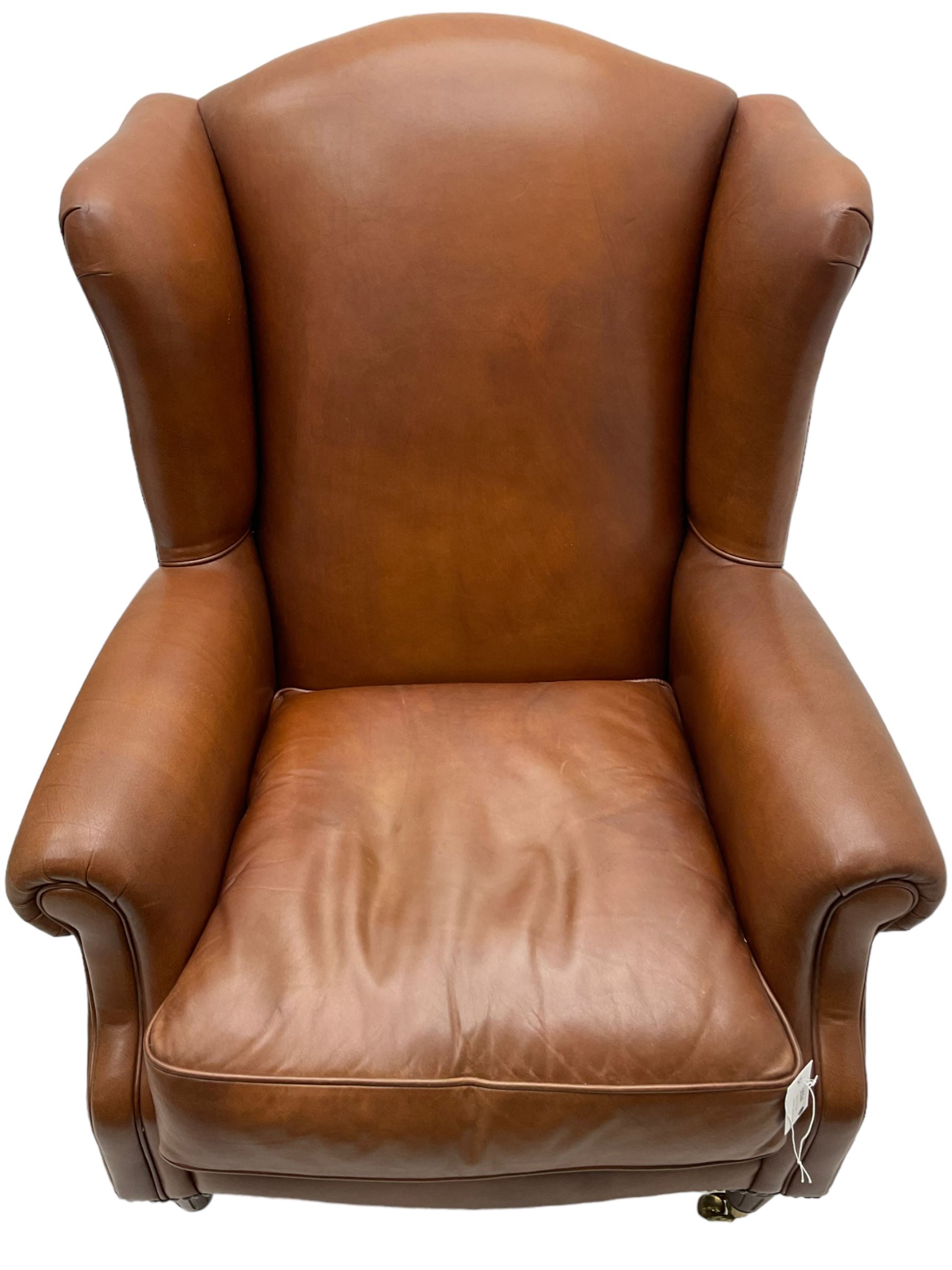 Georgian design wingback armchair, upholstered in brown leather with stud band and piping, turned and fluted front feet on brass cups and castors