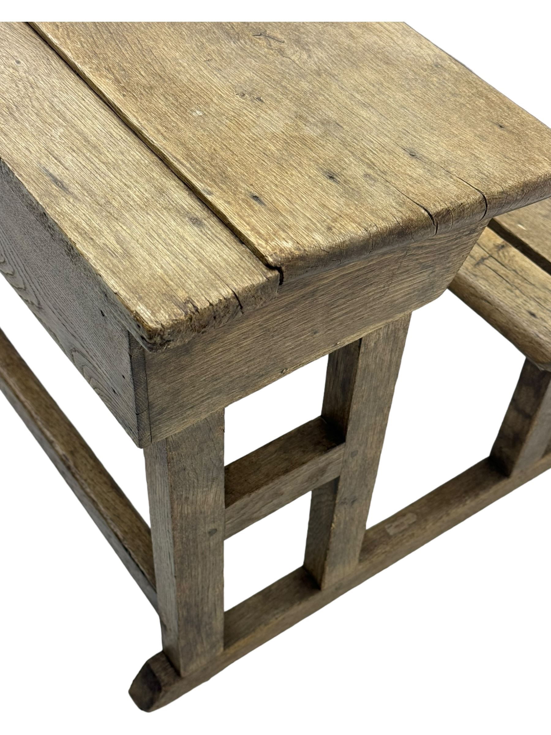 Victorian child's pine double school desk, the writing surface with two inkwells and two shelves underneath, integrated slatted bench seat raised on supports united by stretcher 