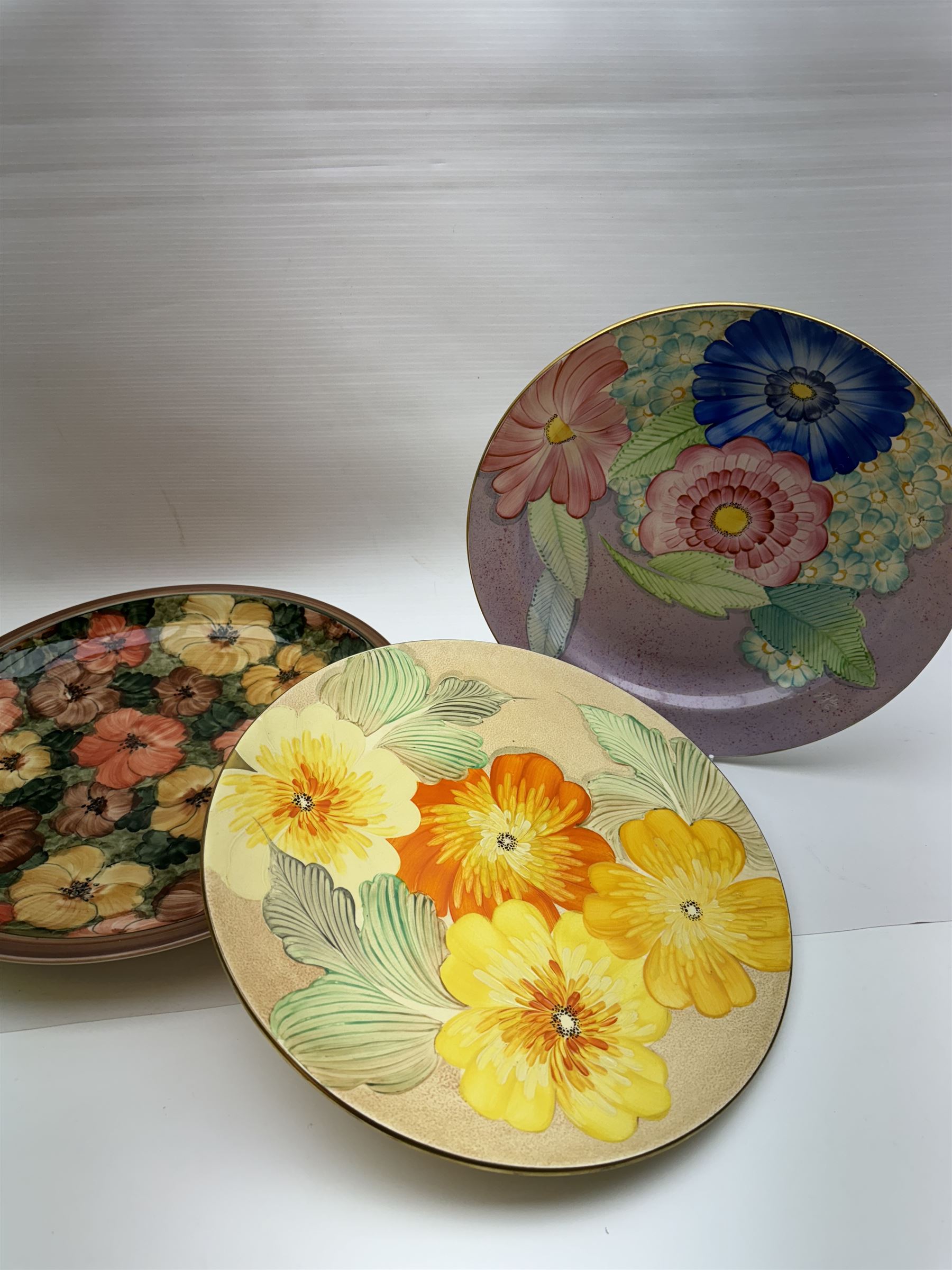 Two Gray's pottery charges, decorated with flowers, together with another charger by Jersey pottery