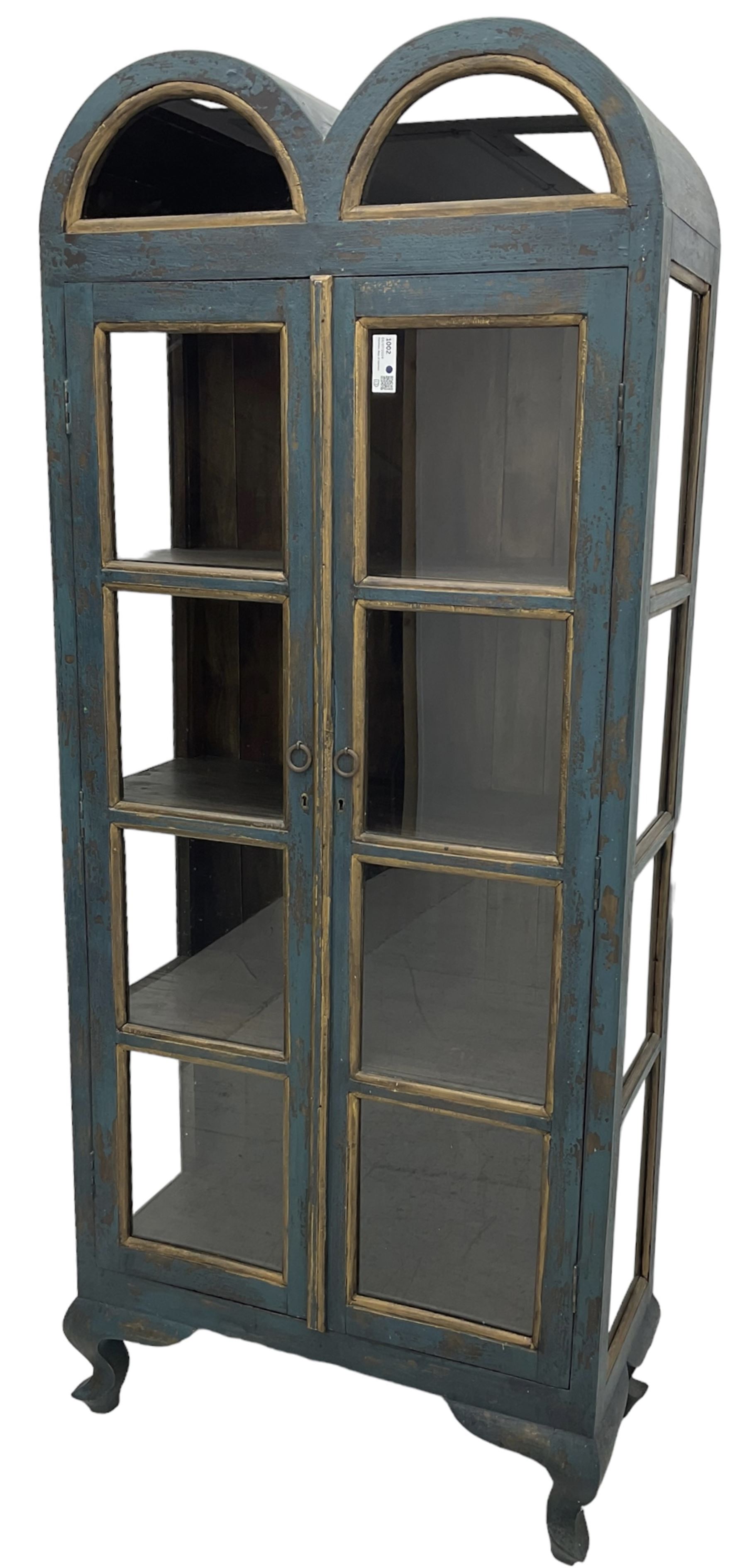 Tall painted glazed display cabinet, double arched top over two glazed doors, fitted with three shelves, in rustic blue paint finish, on cabriole feet