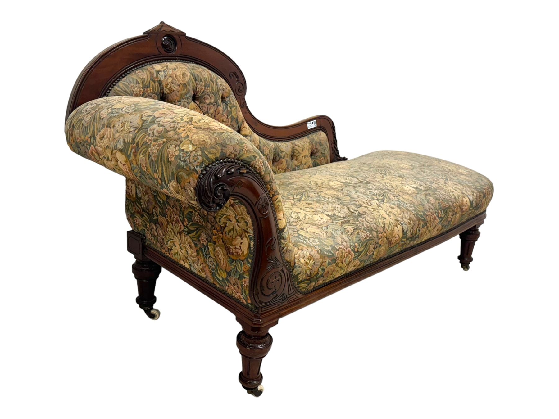 Victorian Aesthetic Movement mahogany framed chaise longue, shaped carved back over acanthus scrolled arm terminal, upholstered in floral patterned tapestry fabric with sprung seat, on turned and fluted supports with castors