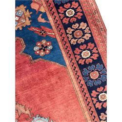 Afghan rust ground carpet, large central lozenge medallion decorated with stylised plant motifs, running water guard stripes enclosing indigo ground border decorated with stylised flower heads