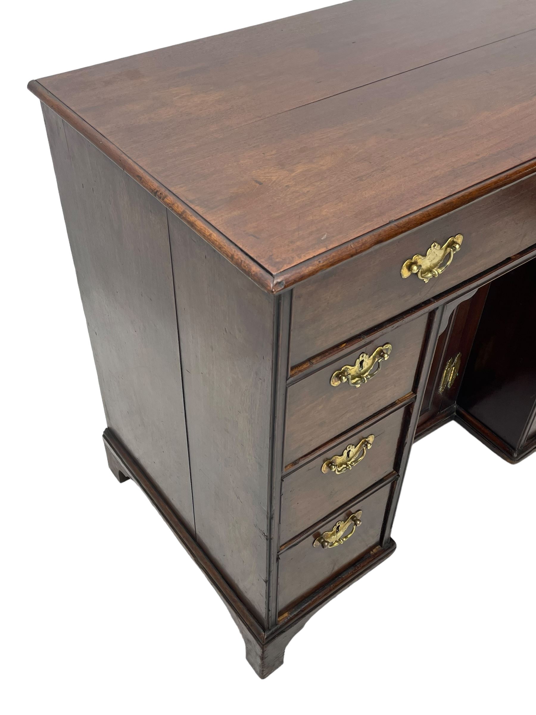 George III mahogany kneehole desk, moulded rectangular top over one long drawer, six short drawers and recessed panelled cupboard, cock-bead moulded frame, fitted with shaped brass handle plates with engraved decoration, on bracket feet 