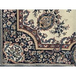 Persian design ivory ground rug, the field decorated with an oval medallion filled with floral motifs and scrolling vines, flanked by floral sprays and corner spandrels with palmette designs, the main border featuring a series of stylised floral patterns against a dark blue ground, enclosed by multiple guard stripes with geometric and floral motifs