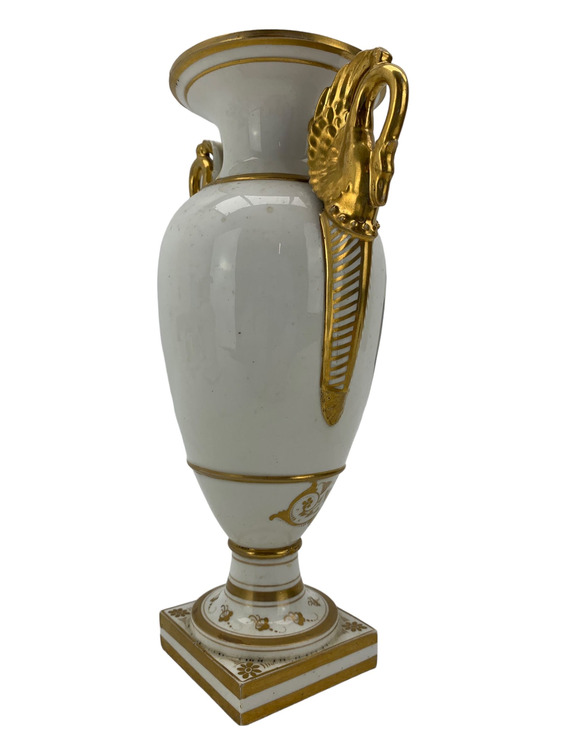 Early 19th century Derby vase, of campana urn form, decorated to one side with a hand painted reserve of a basket of flowers, within a scroll gilt border and twin serpent form handles, H20.5cm together with a Bloor Derby vase, hand painted with figures in a wooded landscape, with twin gilt swan form handles, upon a square pedestal foot, H25cm (2)