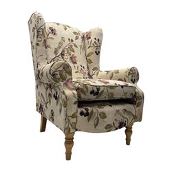 Hardwood-framed wingback armchair, upholstered in cream floral pattern fabric, on turned front feet