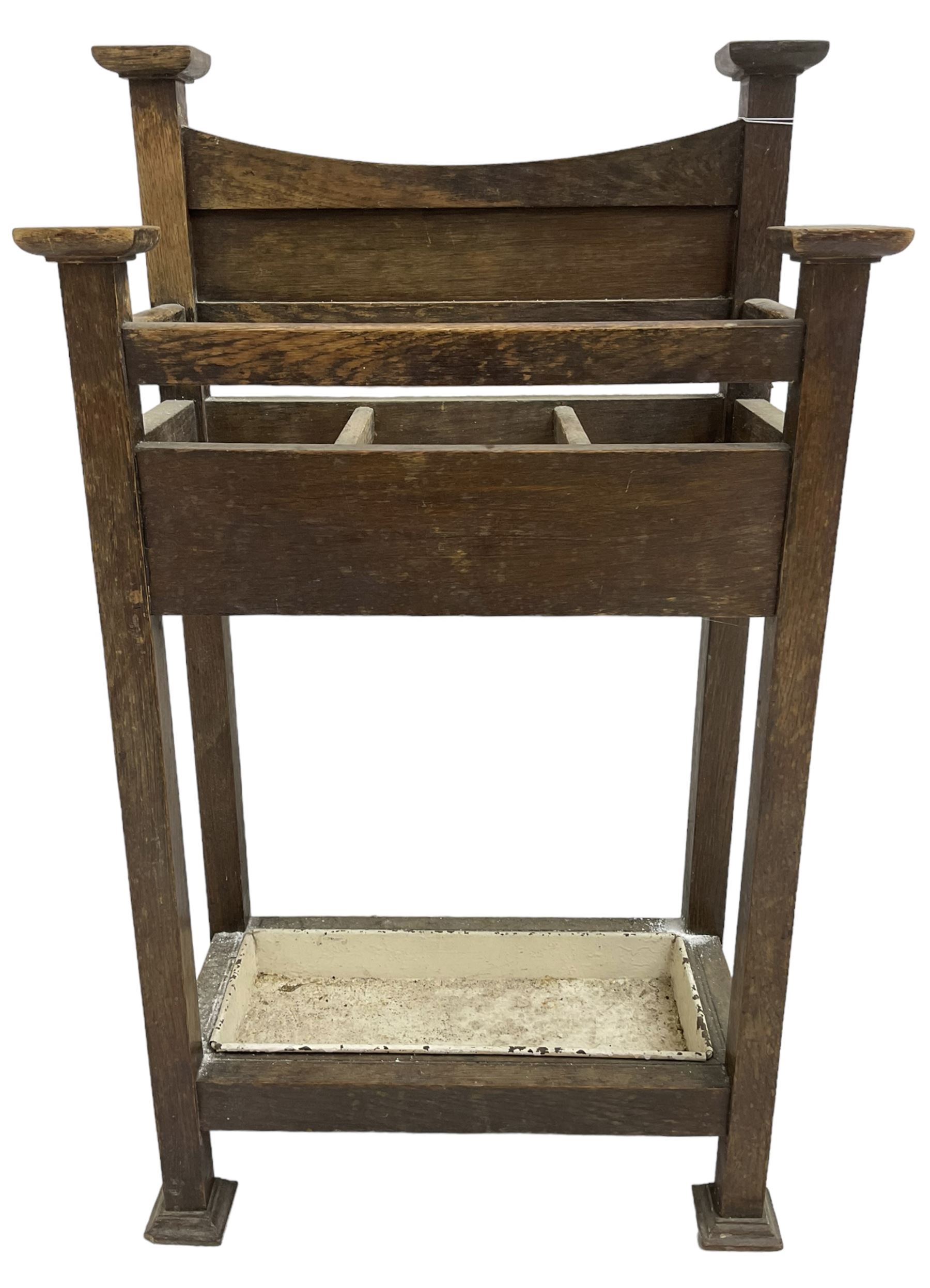 Early 20th century Arts & Crafts oak stick stand, panelled back over three divisions, fitted with metal drip tray, on square supports