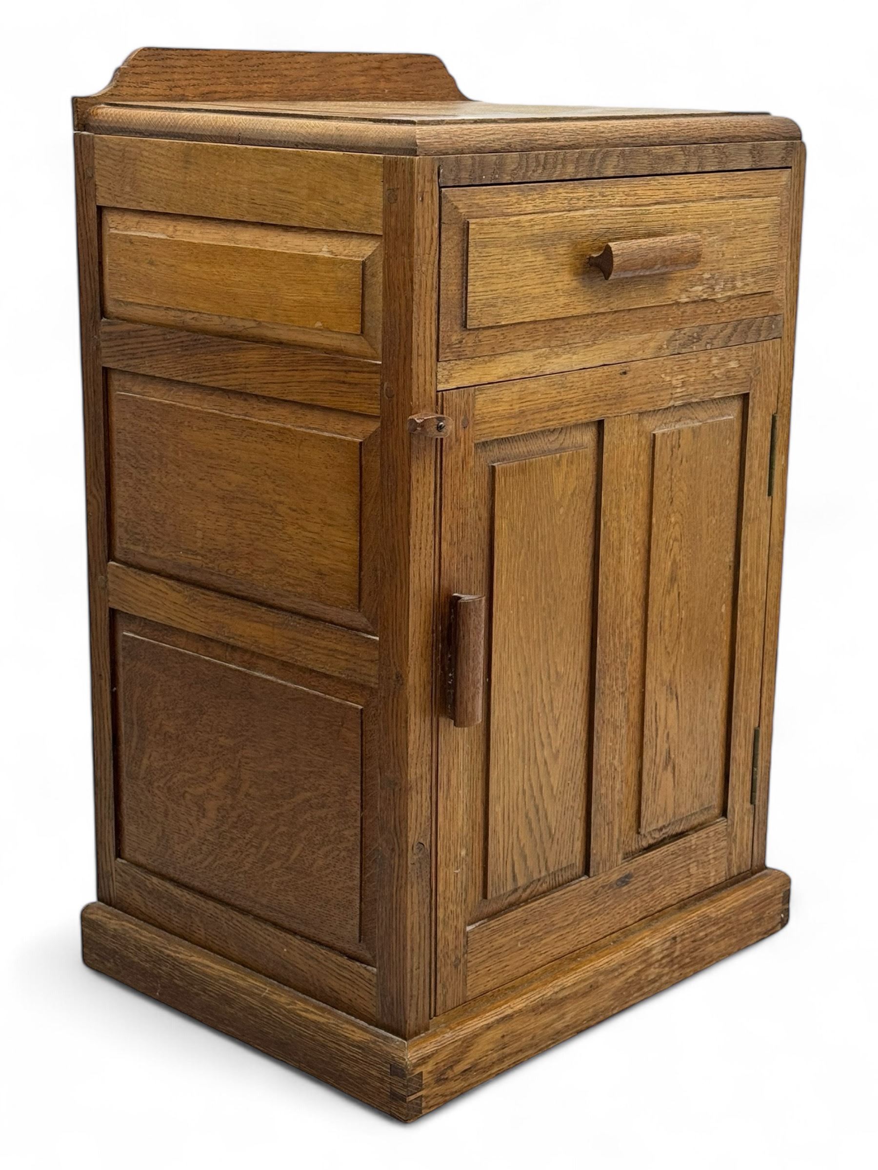 Arts & Crafts period oak bedside cupboard, raised back over moulded top, fitted with single drawer over panelled cupboard, panelled sides, on chamfered plinth base 