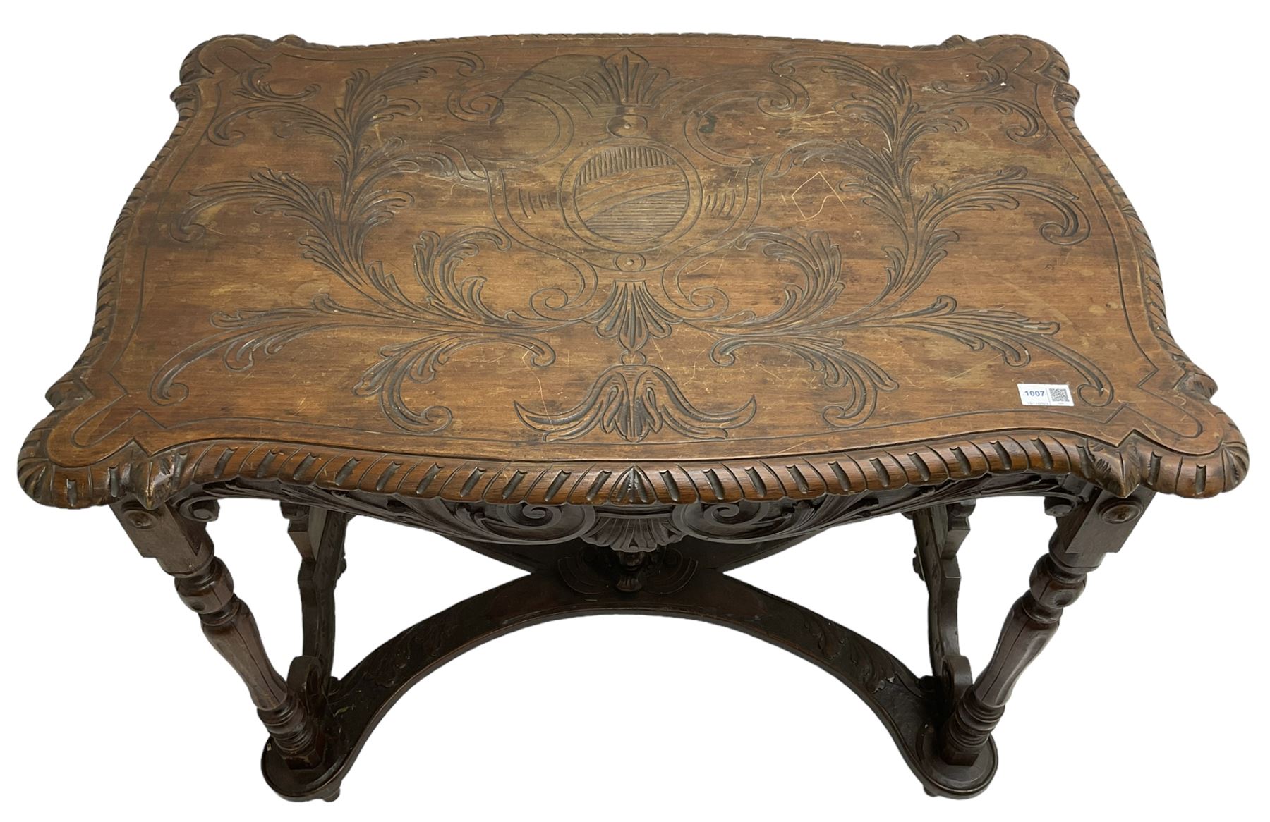 19th century walnut centre table, shaped top carved with central cartouche and extending scrolled foliage, the shaped frieze rails carved with scrolling acanthus leaves, turned supports with central end supports carved with flower heads and scrolls, curved x-framed stretcher carved with a central mask depicting a girl in a bonnet, on turned and carved feet