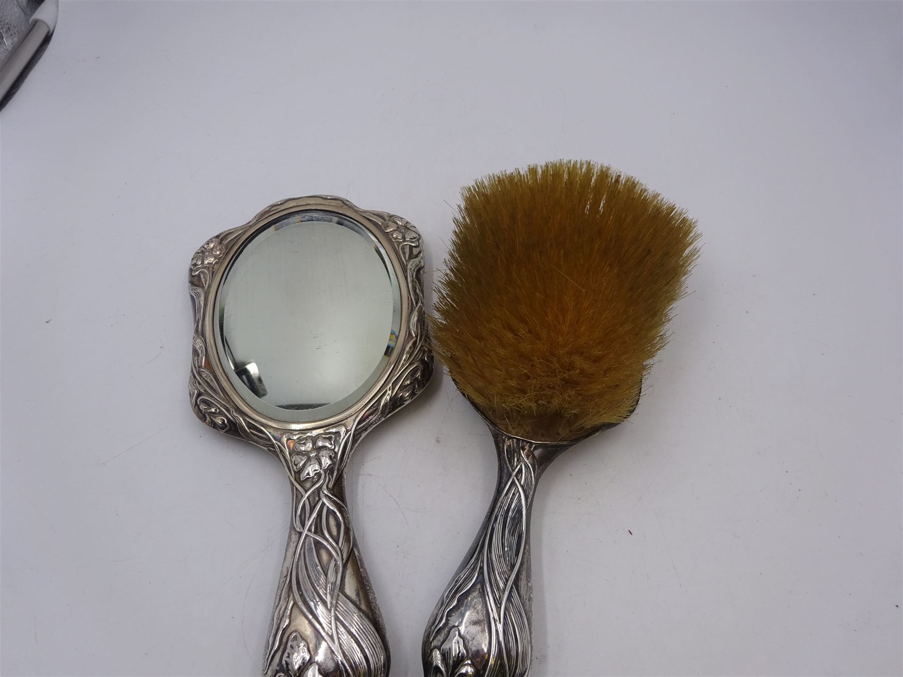 Art Nouveau silver mounted two piece dressing table set, comprising hair brush and hand mirror, each heavily embossed with naturlistic florals and engrved with monograms, hallmarked Walker & Hall, Sheffield 1907