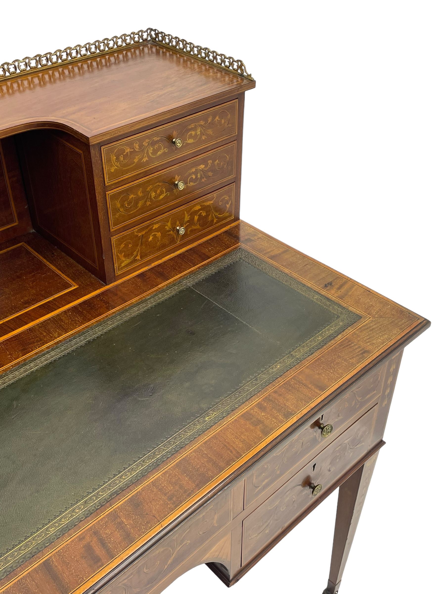 Edwardian inlaid mahogany writing desk, raised galleried back over inlaid central urn with scrolling leafy branches and six small drawers, satinwood banded rectangular moulded top with tooled leather inset, fitted with five drawers, the drawer facias inlaid with scrolling foliage and satinwood banding, square tapering supports inlaid with trailing bell flowers, on brass and ceramic castors 