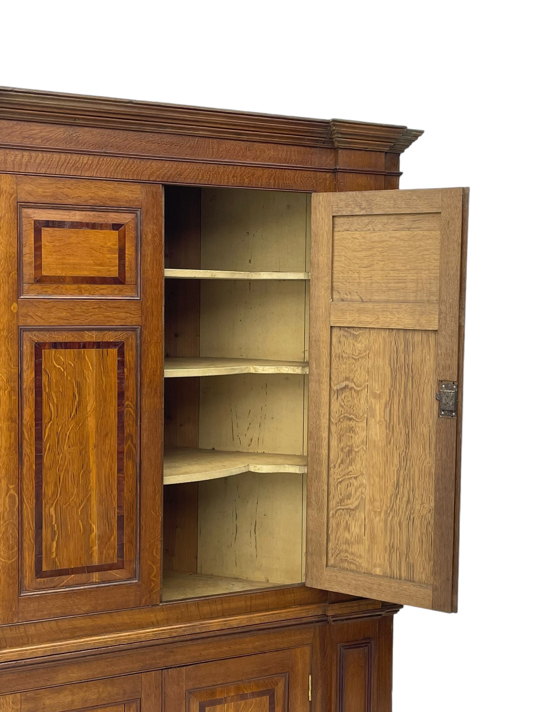 George III and later oak and mahogany banded corner cupboard, moulded cornice over four panelled doors, the door panels inlaid with mahogany bands, projecting square pilasters throughout with applied reeded mouldings, the painted interior fitted with shaped shelves, on moulded plinth base 