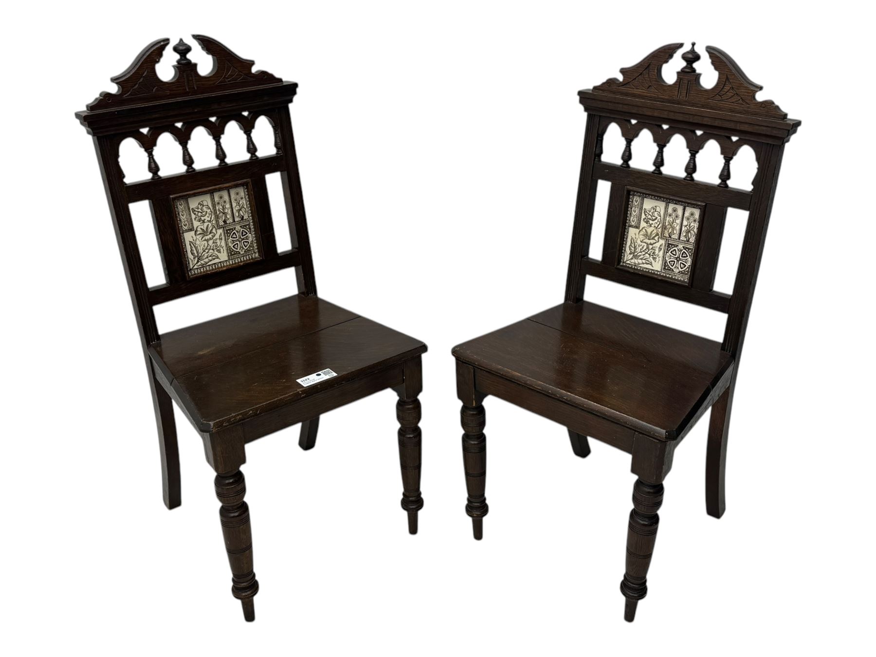 Pair of late Victorian oak hall chairs, shaped pediment over spindle turnings and tiled back, on ring turned supports 