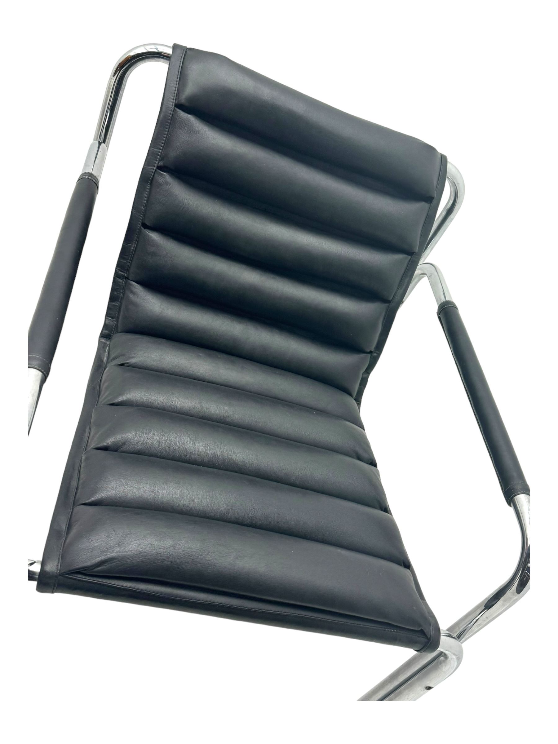 Baroumand Designs - pair of mid 20th century modernist armchairs, slung black leather seat with horizontal channel tufting, tubular chrome frame with curved arms, raised on tubular supports