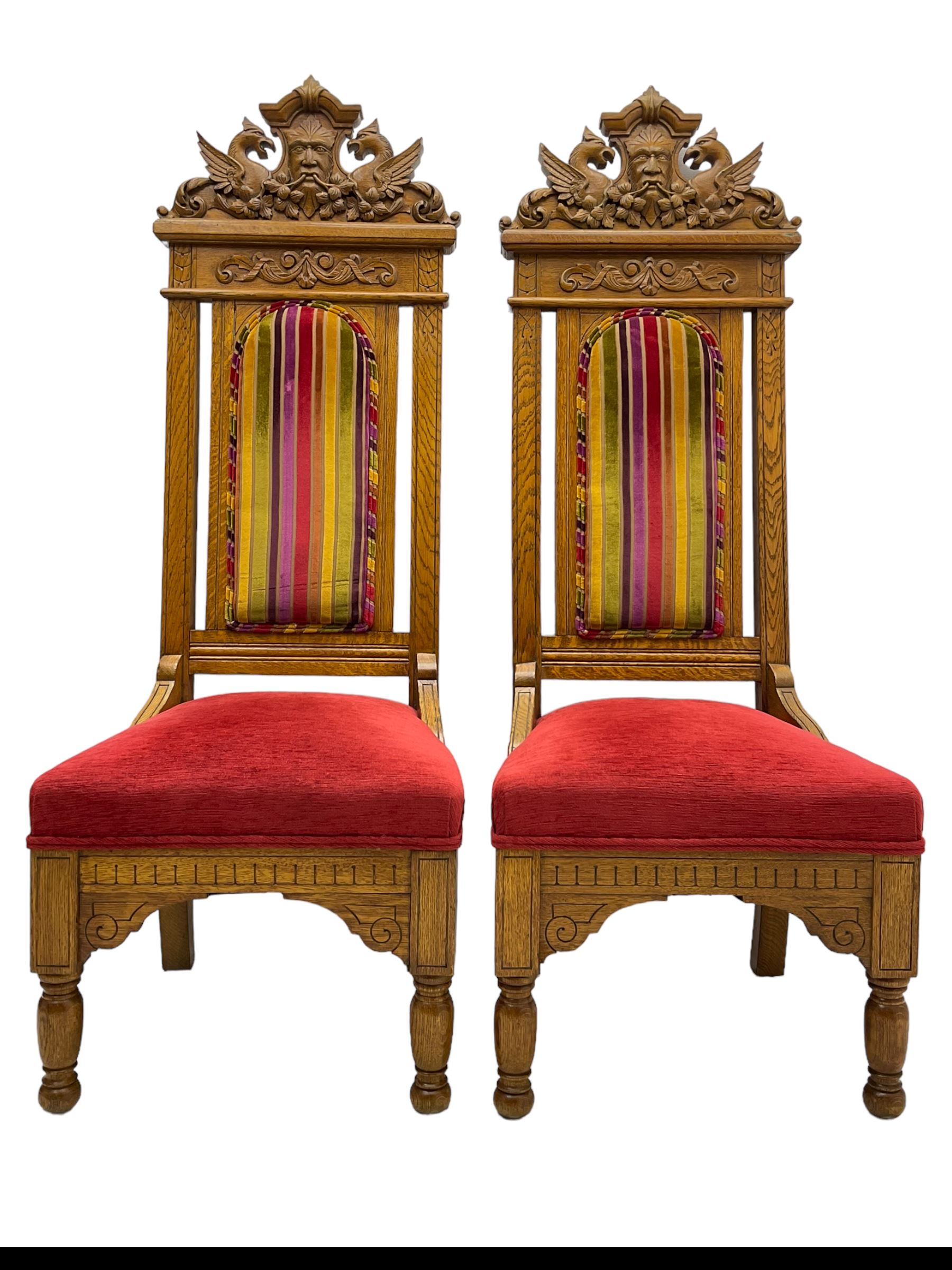 Set of six 20th century Carolean design oak high back chairs, the pediment carved with dragons and central Green Man mask with trailing foliage, the backs upholstered in striped fabric, on turned front supports