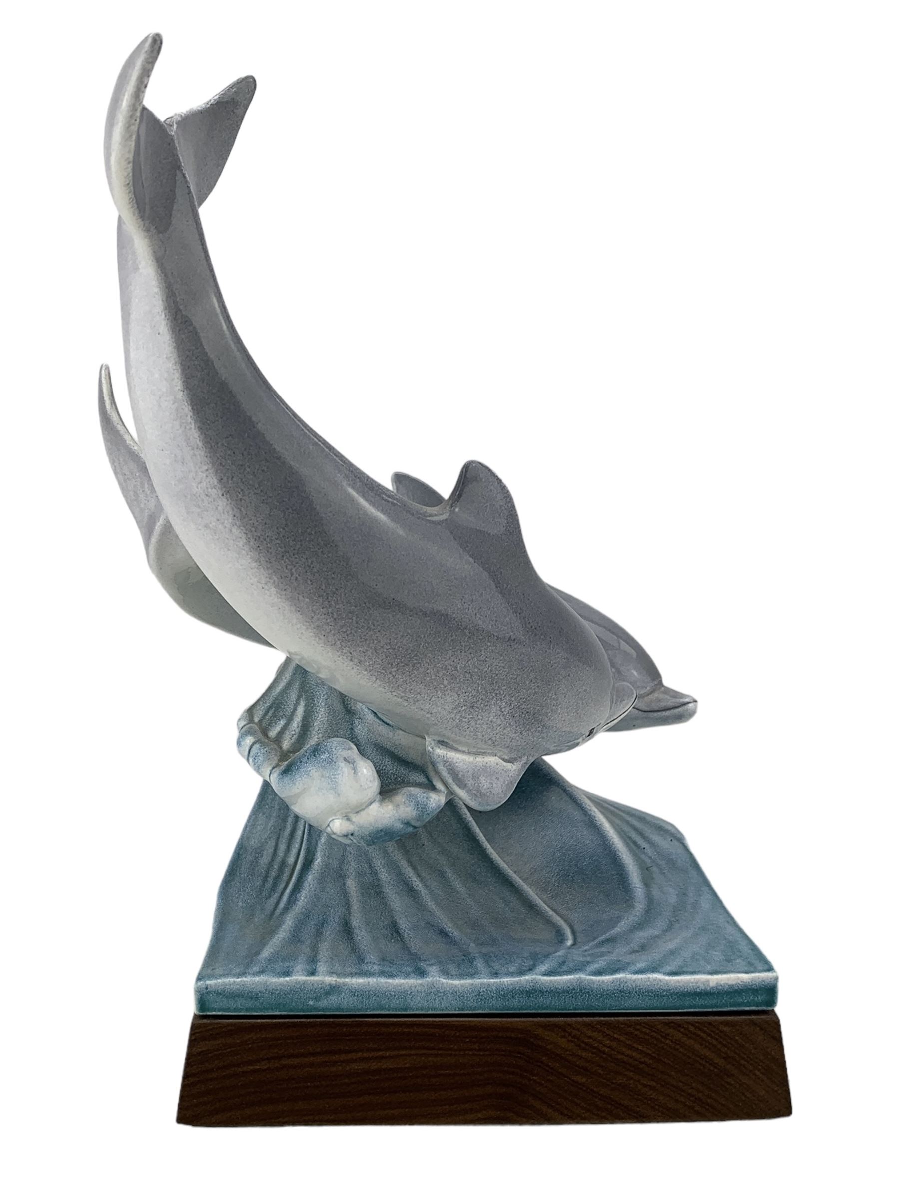 Tony Morris for Poole Pottery, leaping dolphin group, modelled over waves and mounted on a wooden base, H29cm. This model is a duplicate of a sculpture presented to Queen Elizabeth II and the Duke of Edinburgh on their visit to Poole Pottery in 1979, the original cast was destroyed after the production of the duplicate. Provenance: Arnold Smith, Chairman of Pool Potteries Collection