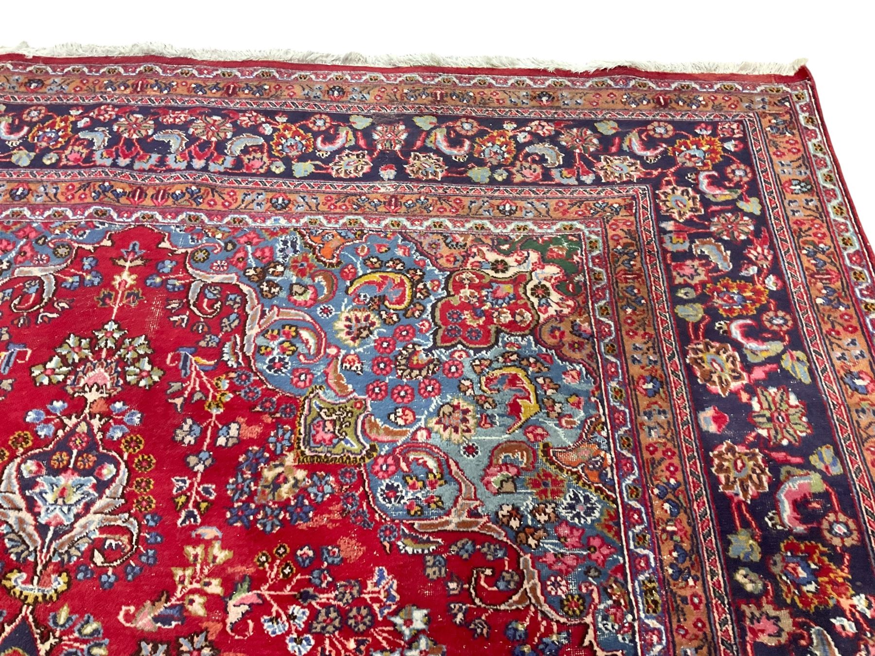 Large Persian Kashan crimson ground carpet, the busy field decorated with a central floral pole medallion surrounded by stylised plant motifs and palmettes with contrasting indigo spandrels, the guarded border decorated with repeating connected foliate designs