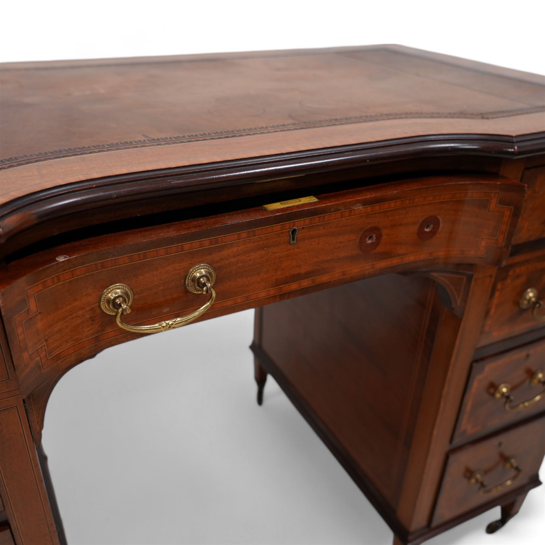 Edwardian inlaid mahogany reverse break bowfront desk, moulded satinwood banded top with inset leather writing surface, fitted with nine drawers, on square tapering feet with brass cups and castors 