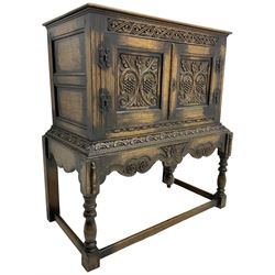 Jacobean Revival carved oak cupboard, moulded rectangular top over S-scroll carved frieze and two doors, the panelled doors carved with stylised plant motifs, on stand decorated with lunettes and shaped apron with hanging turned pendant, on turned supports united by stretchers 