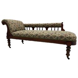 Late 19th century walnut framed chaise longue, upholstered in floral pattern fabric, rolled back rest and turned balustrade back, on turned feet with brass and ceramic castors 