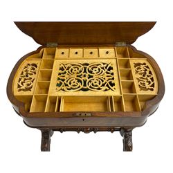 Victorian inlaid walnut sewing table, the shaped hinged lid with quarter matched veneers inlaid with trailing foliate, birdseye maple interior fitted with lidded compartments and sunken storage well, on twin pillars carved with foliage joined by turned stretcher, splayed supports carved with scrolls and foliage, on brass and ceramic castors