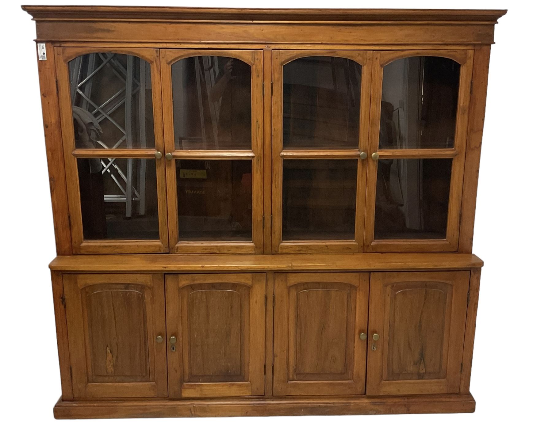 Mid-to-late 20th century Burmese teak wall cabinet, four glazed doors over four panelled doors, on moulded plinth base 