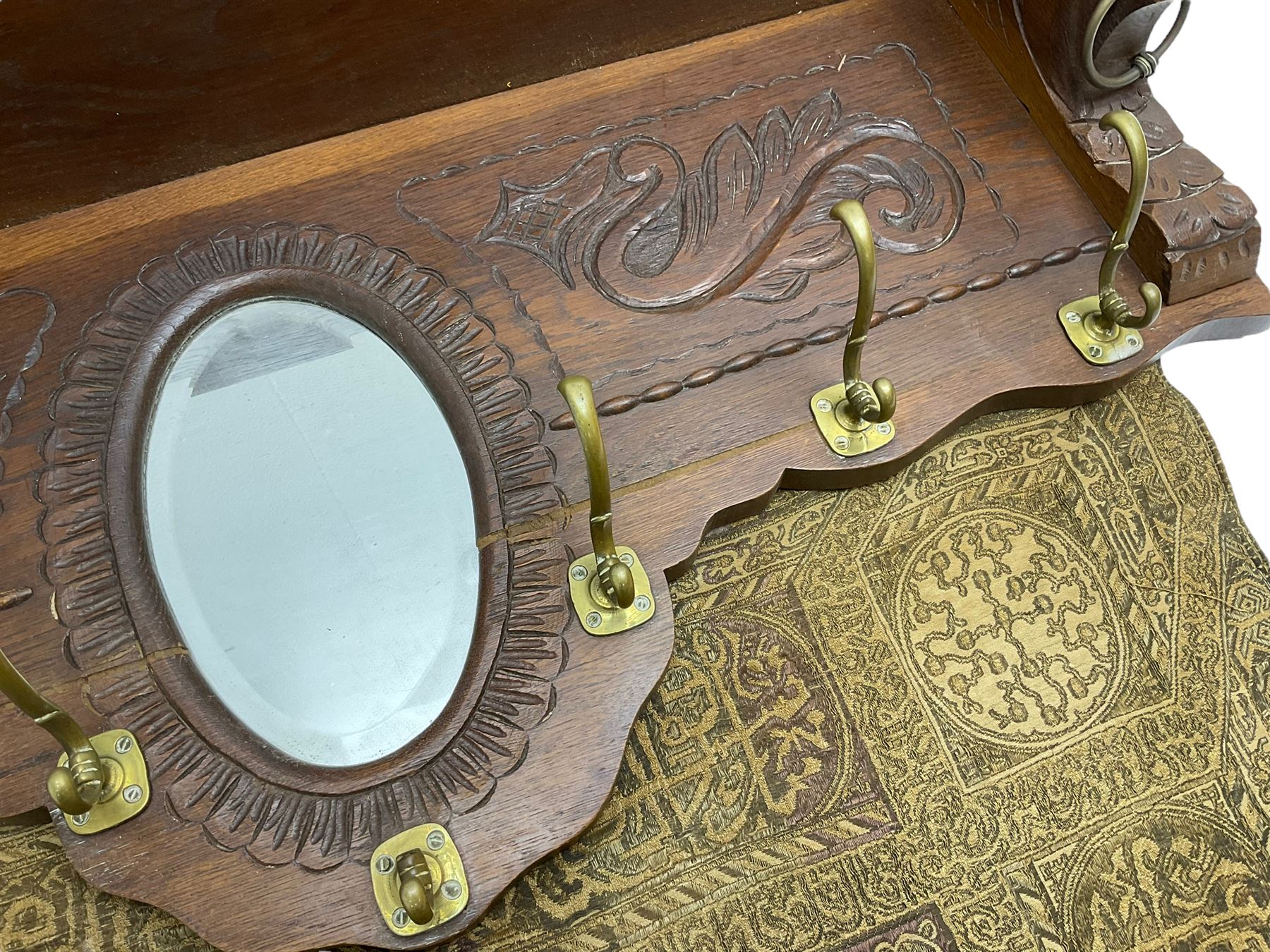 Late 20th century oak wall hanging coat rack, central bevelled oval mirror in foliate carved surround, decorated with S-scrolls and lion masks, fitted with needlework hanging 