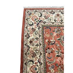 Persian Kashan peach ground rug, the field decorated with swirling leafy branches and stylised plant motifs, ivory ground border with trailing foliate design interspersed with flower heads, within guard stripes 