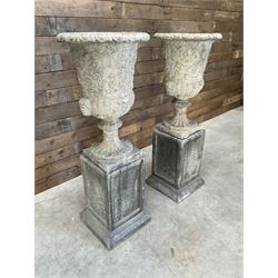 Pair of Georgian design cast stone garden urns, egg and dart rim with raised floral motifs, pedestal base terminating on square plinth, raised on square block plinth