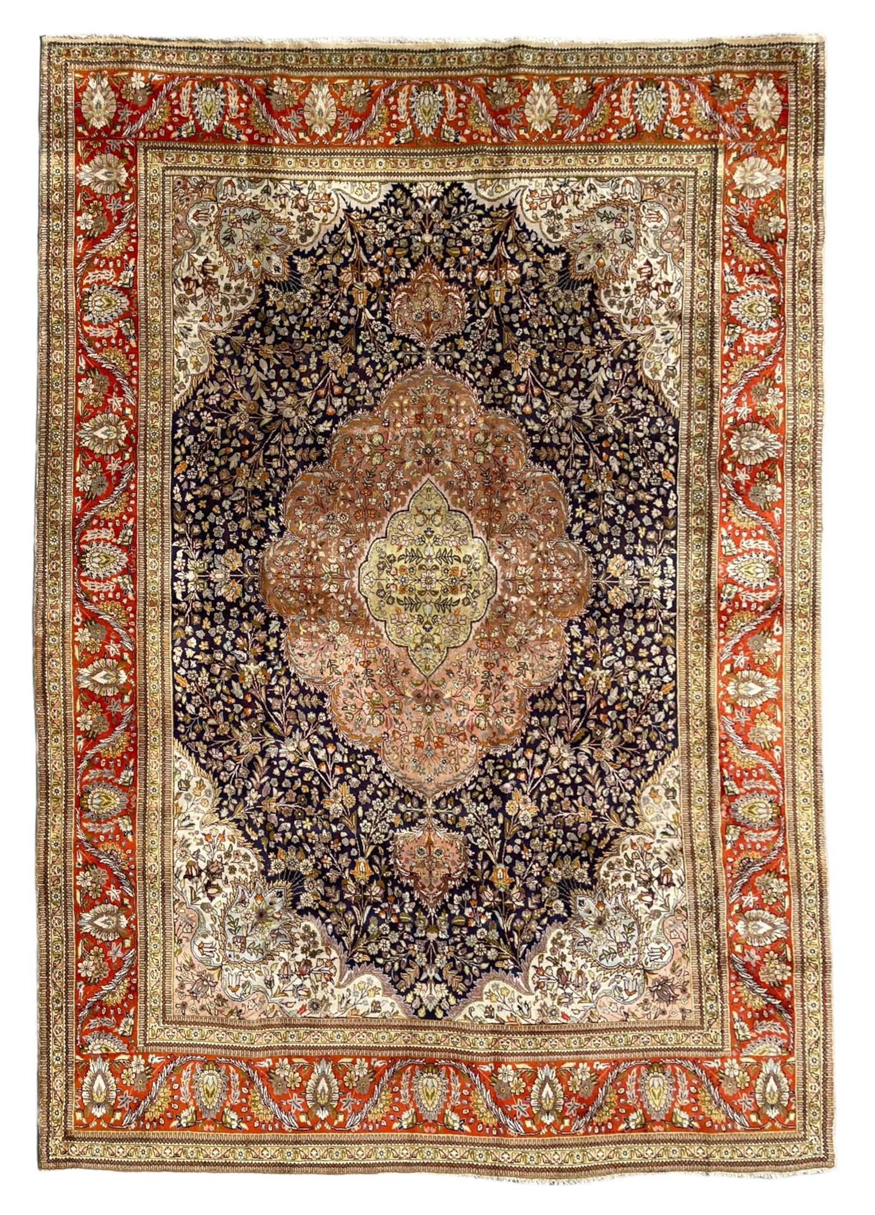 Persian Kashan, scalloped central medallion on indigo ground field, decorated profusely with branch shoots with floral motifs, pale ground spandrels decorated with stylised flower head motifs, crimson ground border decorated with repeating palmettes and trailing leafy branches, within multiple guard stripes 