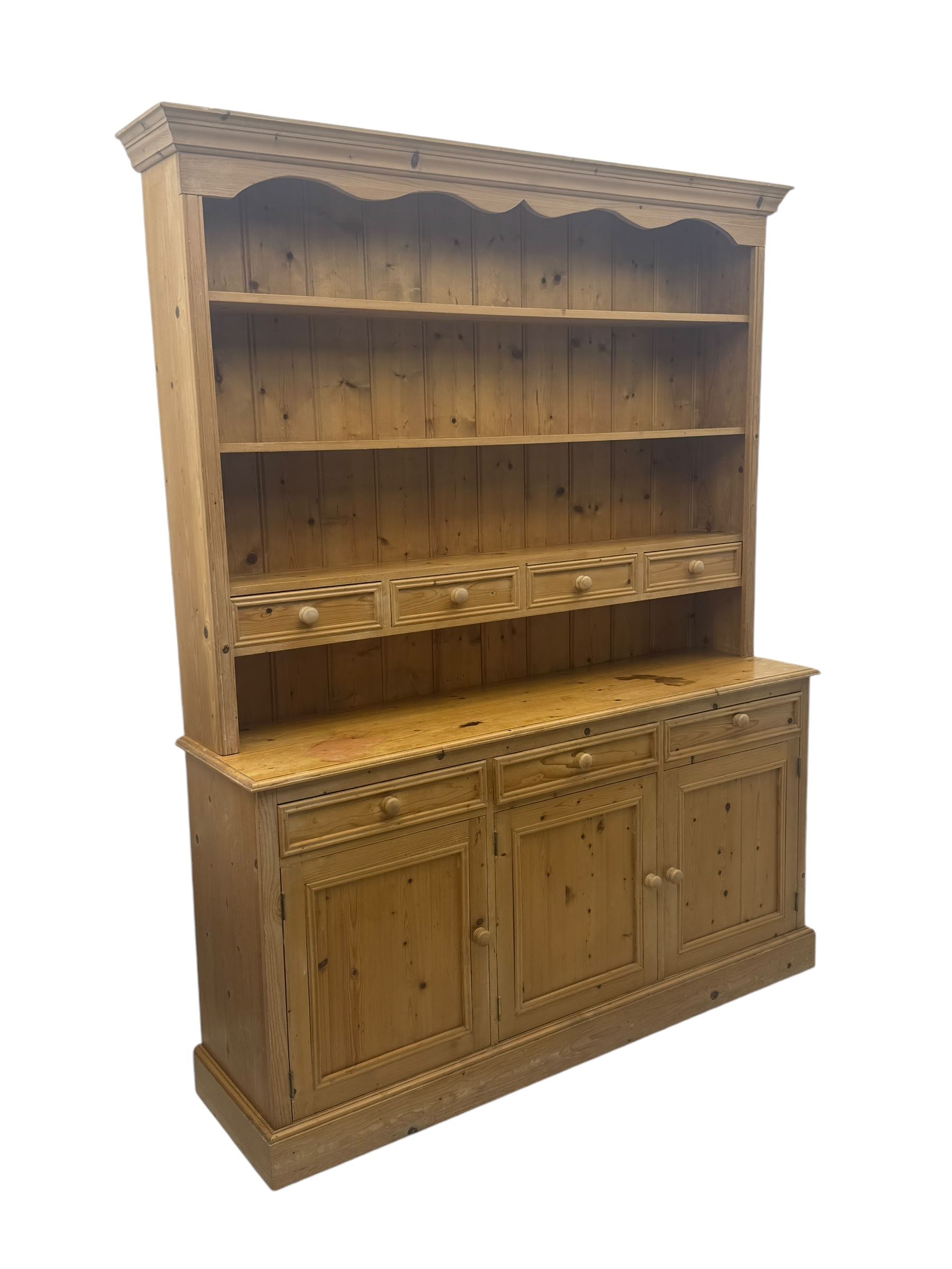 Traditional design waxed pine dresser, upper section with moulded cornice over scalloped frieze, fitted with two open shelves and four drawers, lower section with three drawers over three panelled cupboards, on plinth base