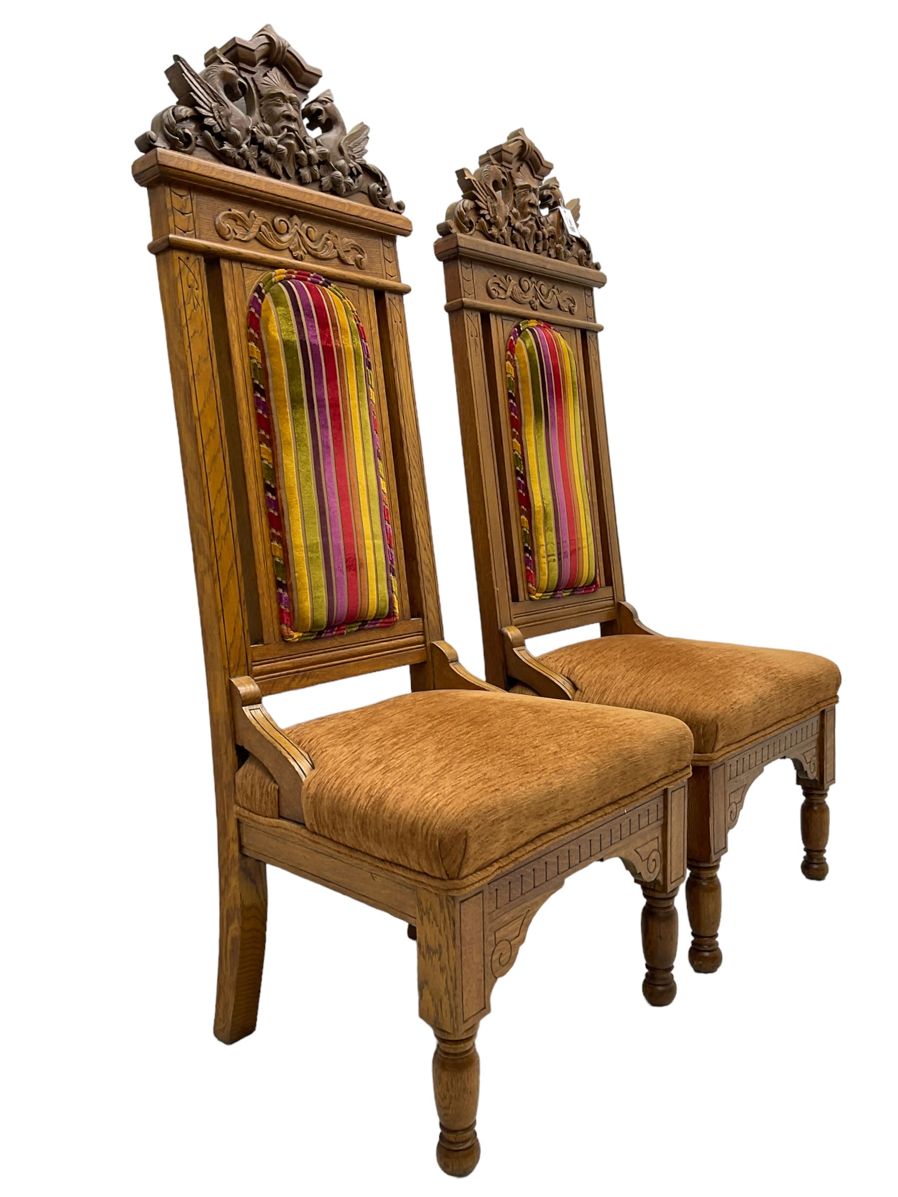 Set of six 20th century Carolean design oak high back chairs, the pediment carved with dragons and central Green Man mask with trailing foliage, the backs upholstered in striped fabric, on turned front supports