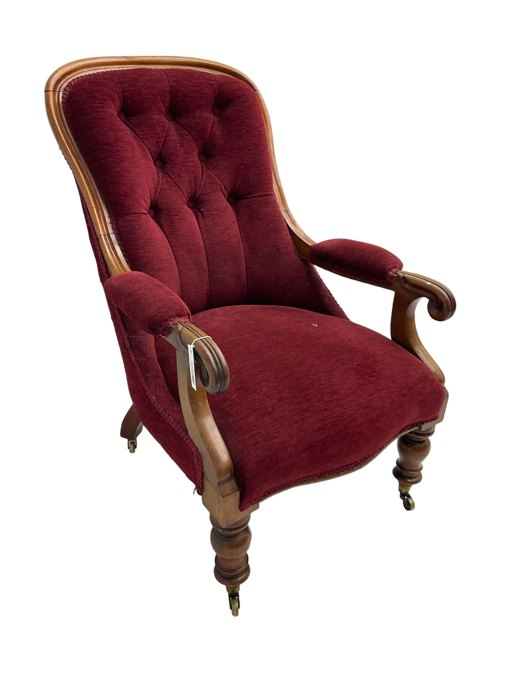 Victorian mahogany framed open armchair, upholstered in buttoned red fabric, the arm terminals carved with scrolls, on turned front supports with brass cups and castors