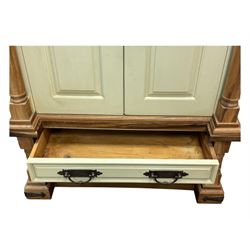 Hardwood and cream painted kitchen larder cupboard, sloped pediment over two panelled doors, the interior fitted with slides, drawers and storage shelves, two long drawers below, mounted by turned pilasters, on metal bound moulded plinth base