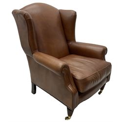 Georgian design wingback armchair, upholstered in brown leather with stud band and piping, turned and fluted front feet on brass cups and castors