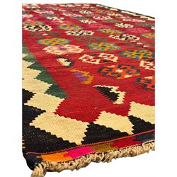 Southwest Persian Qashqai Kilim red ground rug, the central field adorned with rows of multicolored hexagonal medallions with geometric patterns, the border featuring alternating black and white stepped diamonds, narrow band to one end decorated with multicoloured geometric figures