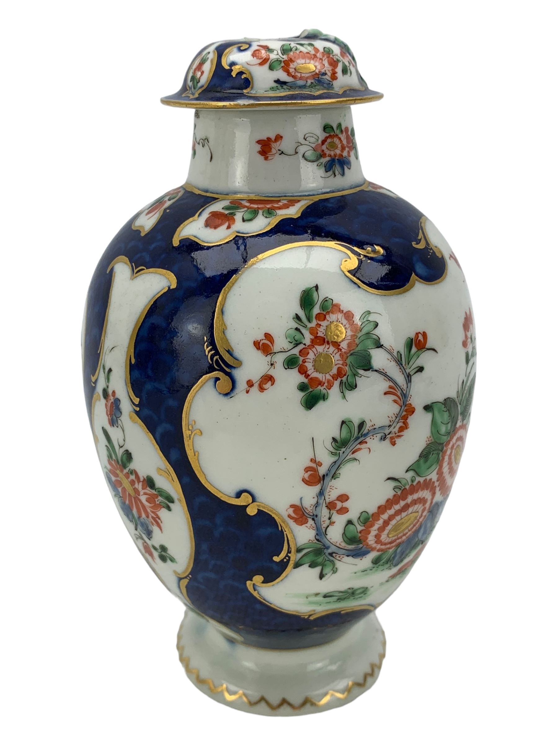 18th century Worcester tea caddy, of oval form and painted in the Kakiemon palette with reserves of flowers against a blue scale ground, H14cm together with a similar Worcester circular dish, painted with floral sprays, within a scalloped edge, blue crescent mark beneath, D19cm (2)