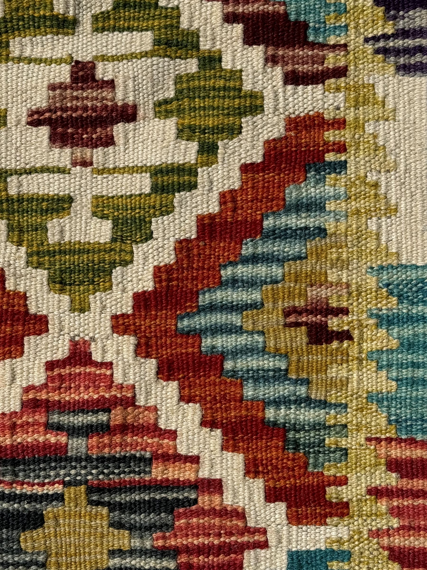 Chobi Kilim ground runner, the field decorated with a geometric pattern of coloured diamonds and triangles, each containing stylised motifs, the shorter ends enclosed by a plain border, and the longer sides with a multicoloured border

