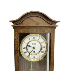 Commiti of London -  three train spring driven 8-day wall clock in an oak case, with a fully glazed door and curved pediment, two part dial with Roman numerals, spade hands and gridiron pendulum, rack movement chiming the hours and quarters on 5 gong rods. With key.